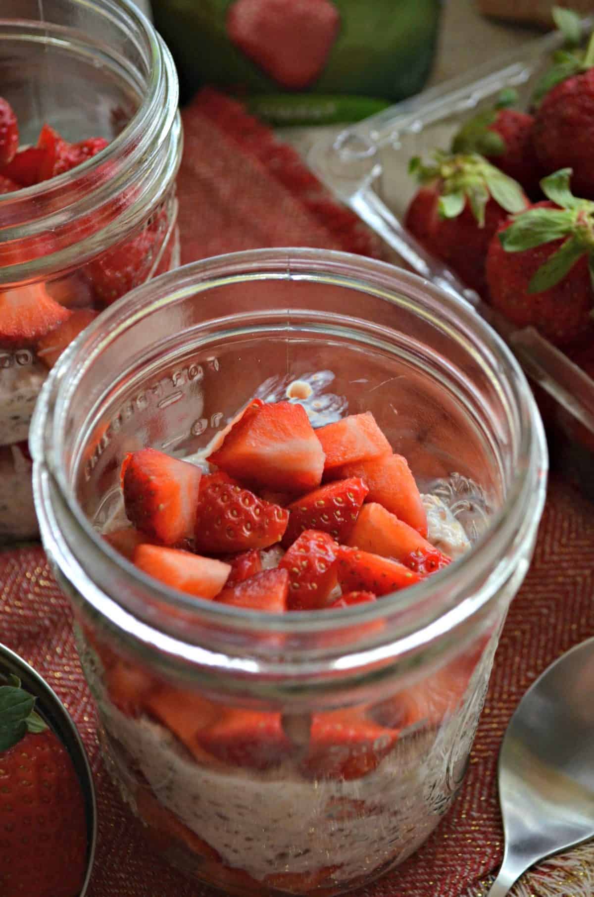 close up top view of 2 small mason jars filled with oatmeal looking substance and chopped strawberries.