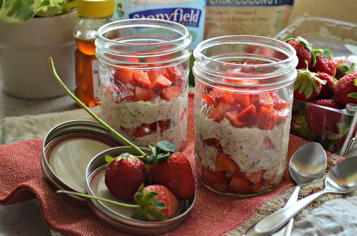 2 small mason jars filled with oatmeal looking substance and fresh chopped strawberries in 3 layers.