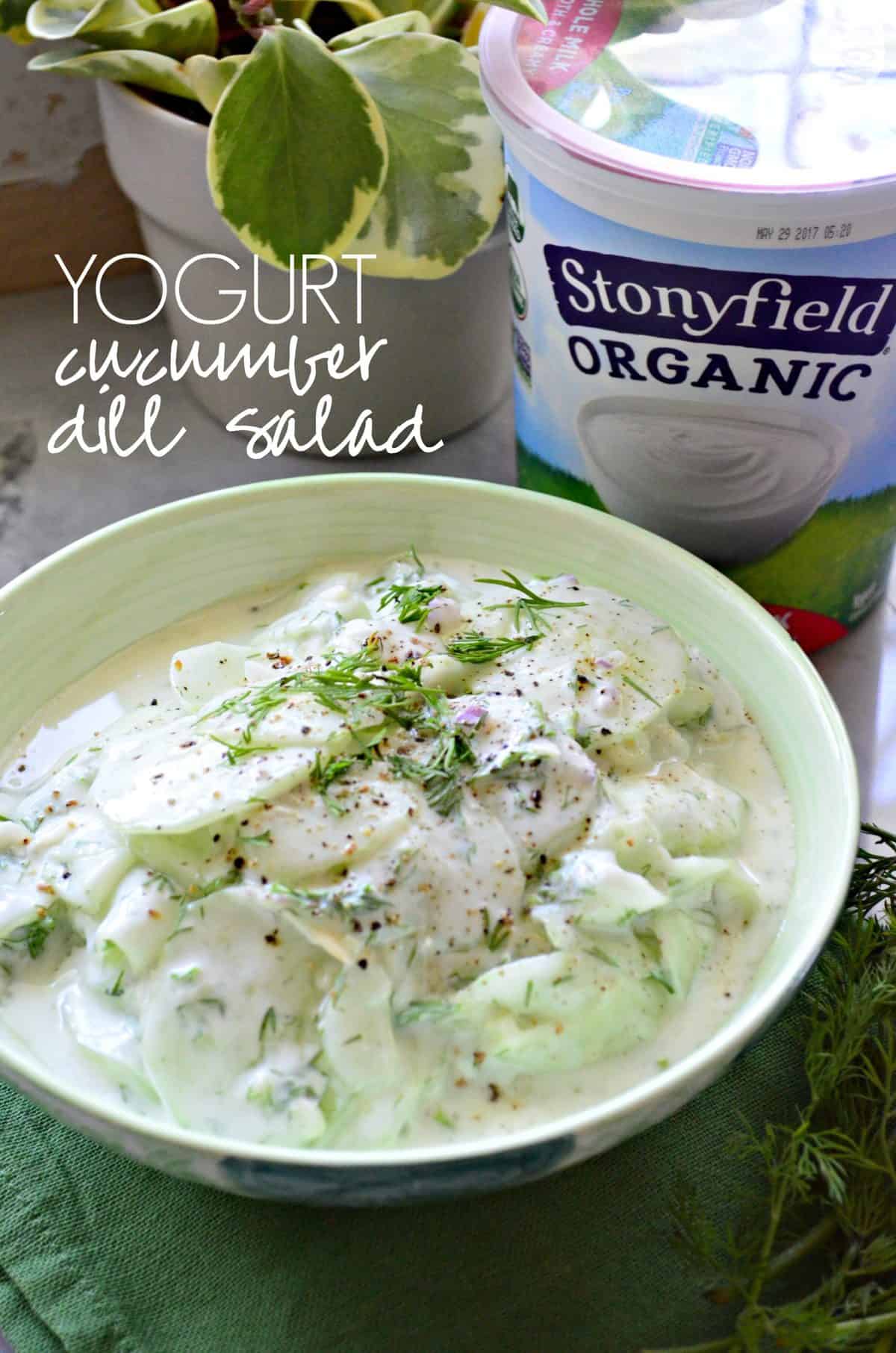 green bowl filled with yogurt dill cucumber salad on countertop in front of stonyfield organic yogurt with title text.
