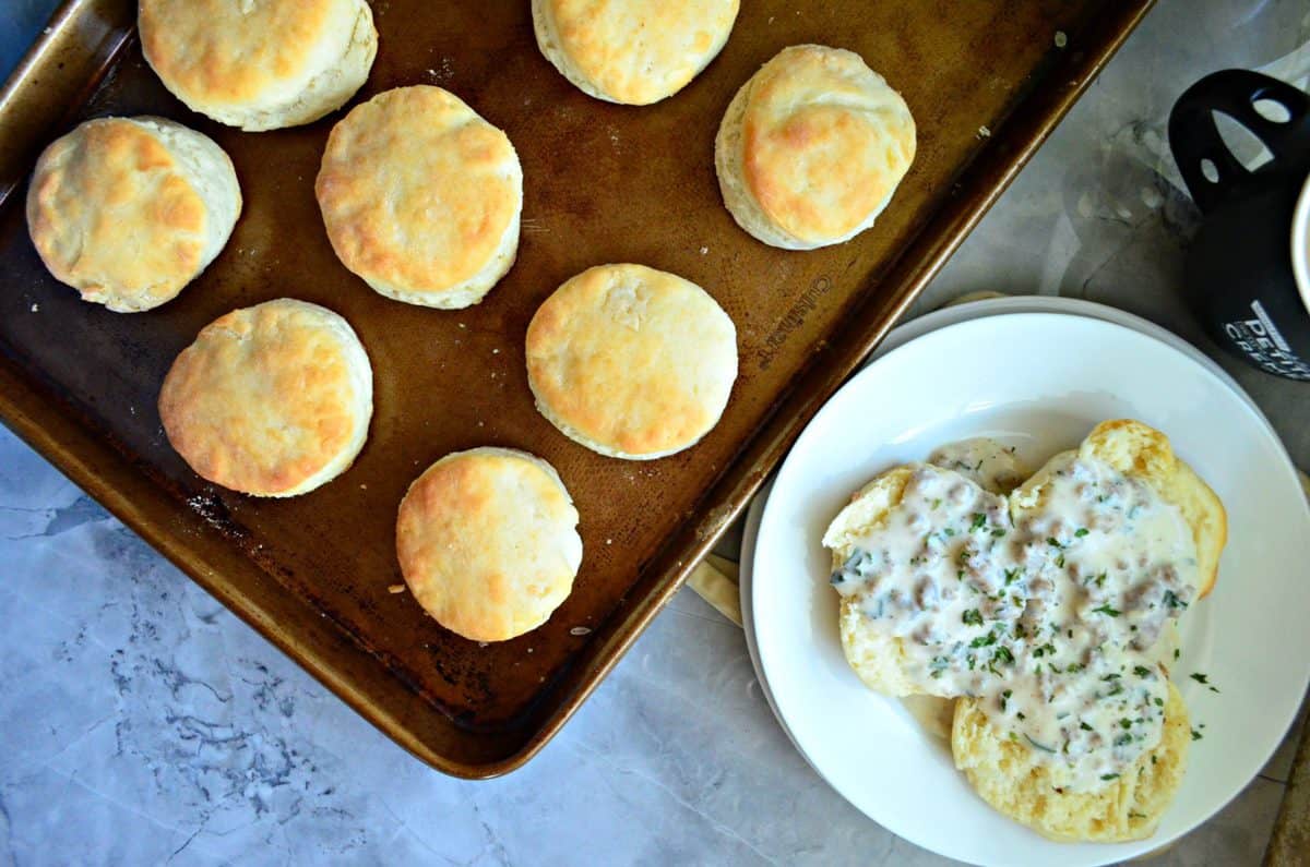 Top view of cooked biscuits with a plate of biscuits and gravy next to it.