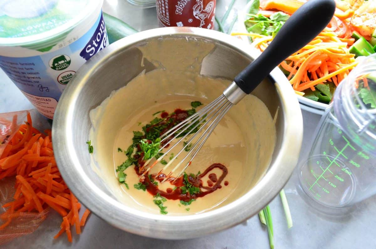 top view of bowl with yogurt, sriracha, and herbs  about to be mixed with wisk.