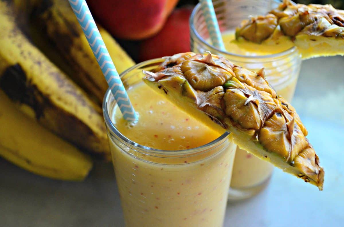 top view of 2 glasses of Pineapple Banana Peach Smoothie on countertop with with fruit burred in background.