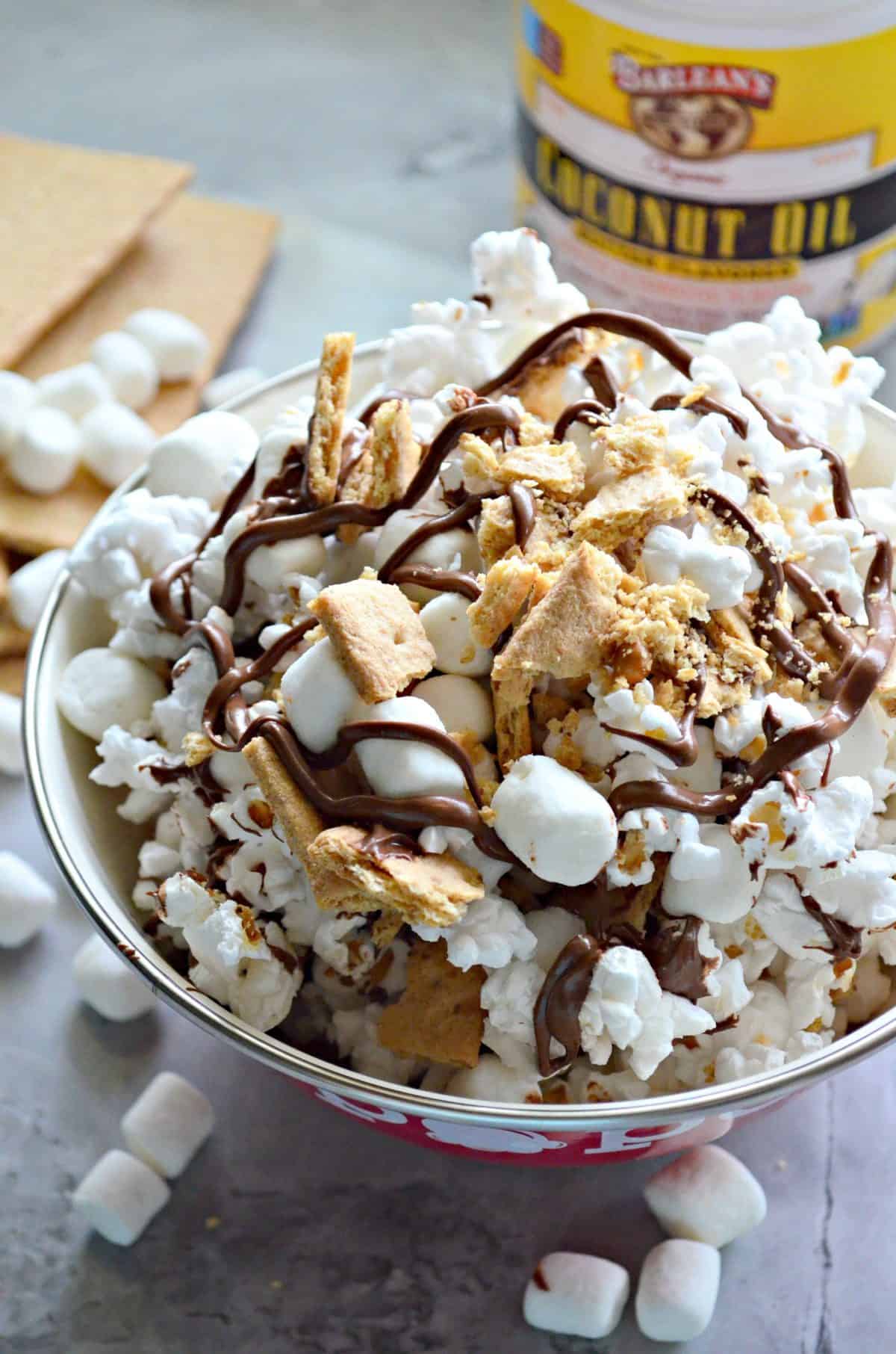 close up bowl of popcorn with graham crackers, chocolate drizzles, and mini marshmallows with title text.