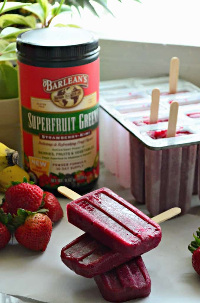 3 beet red popsicles stacked on parchment paper on countertop with popsicle tray in background.