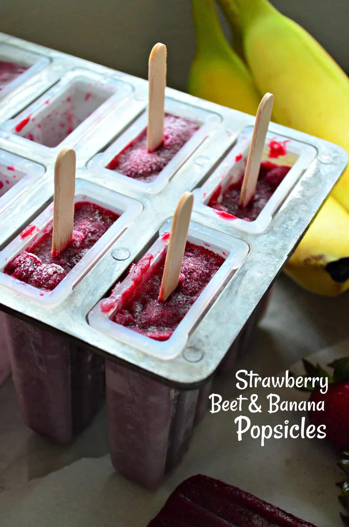 Beet red popsicles in popsicle tray with wooden sticks sticking out next to fresh bananas with title text.