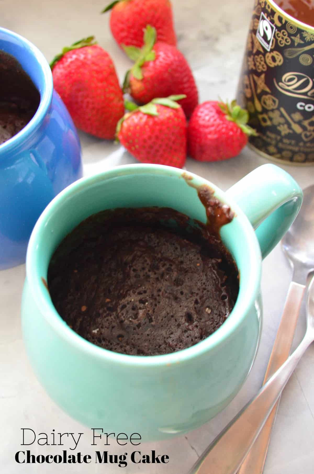 closeup of turquoise mug filled with brown cake with strawberries blurred in background and title text.