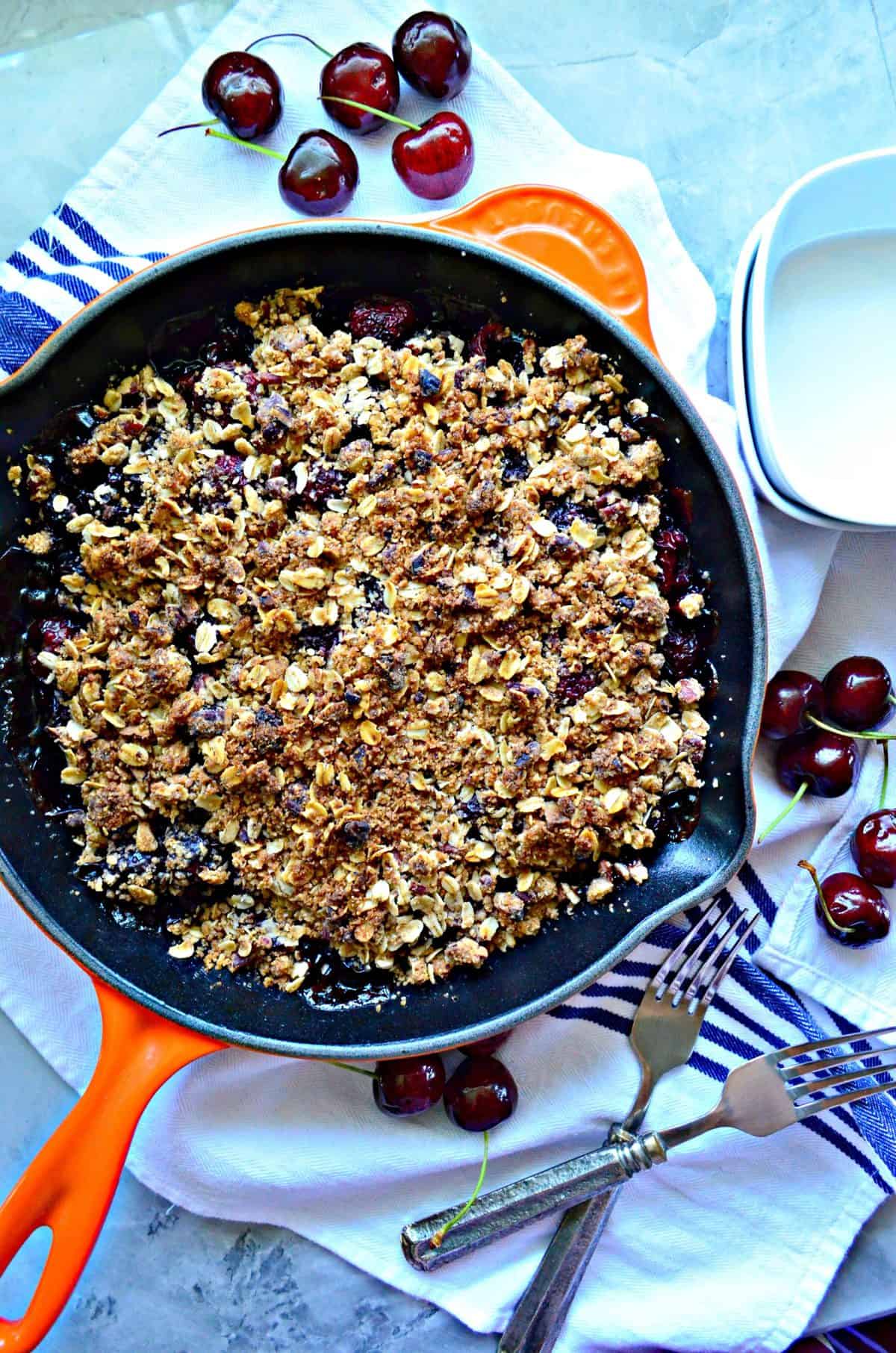 top view of cherry crisp topped with golden brown oatmeal in skillet near fresh cherries.