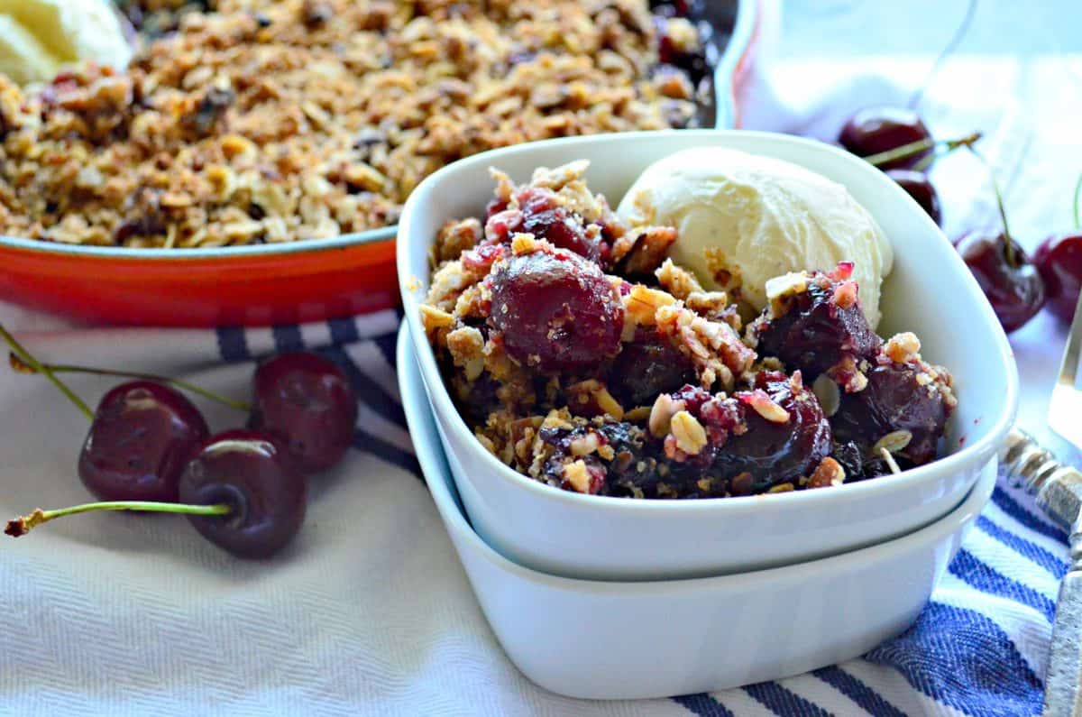 Dairy-Free Skillet Cherry Crisp in small white bowl with scoop of white creamy looking substance.