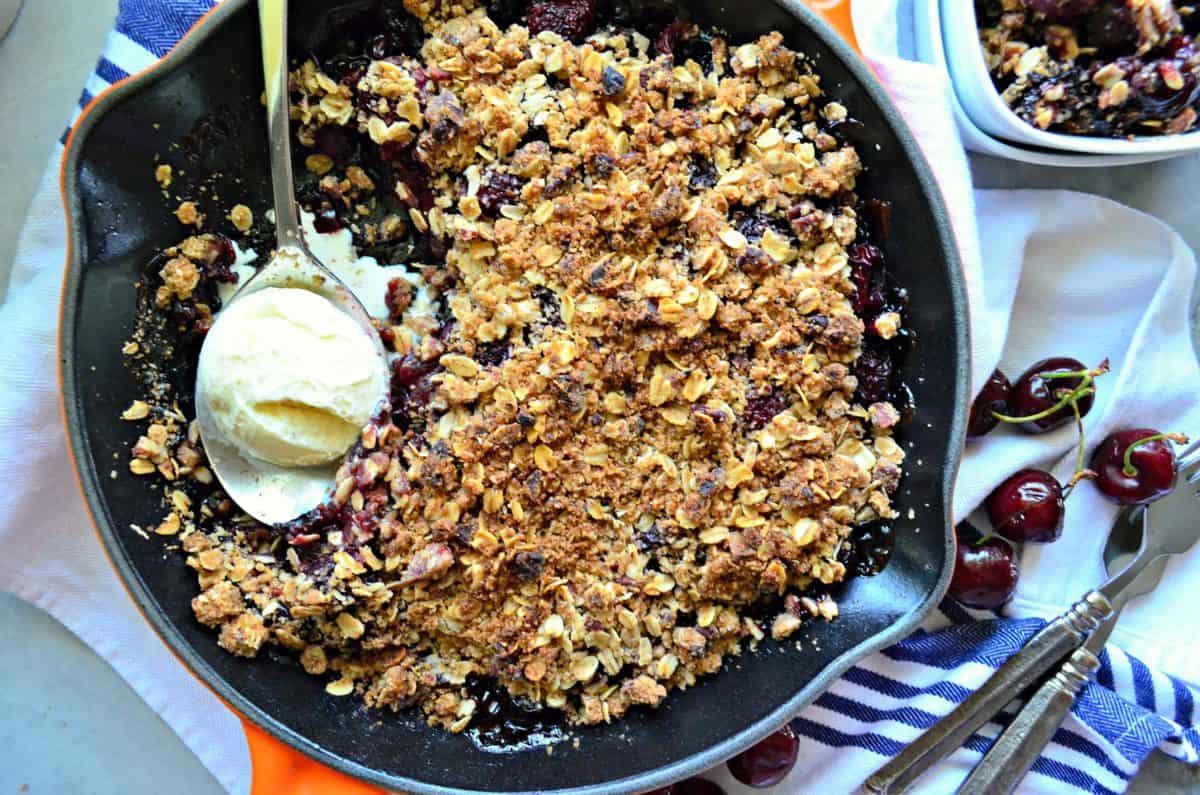 top view of cherry crisp topped with golden brown oatmeal with spoonful of ice cream in skillet.