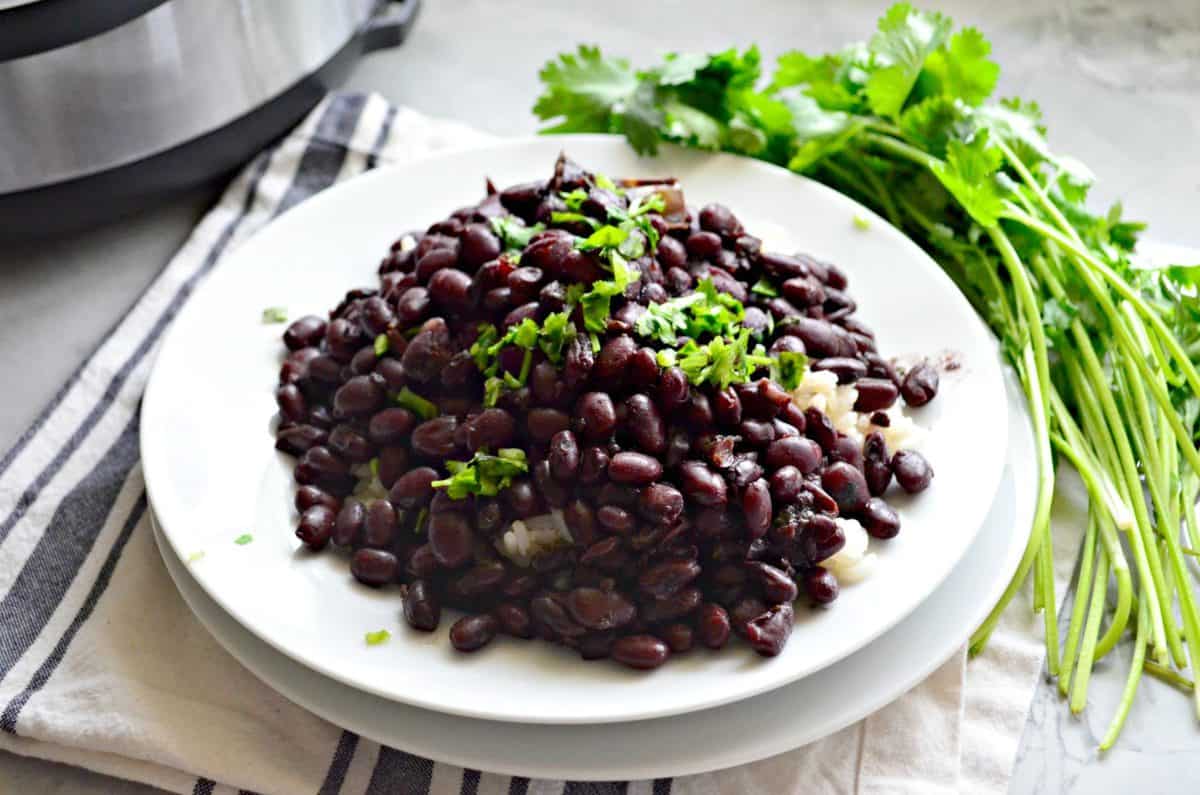 black beans with chopped fresh cilantro over bed of white rice on white plate by fresh cilantro.