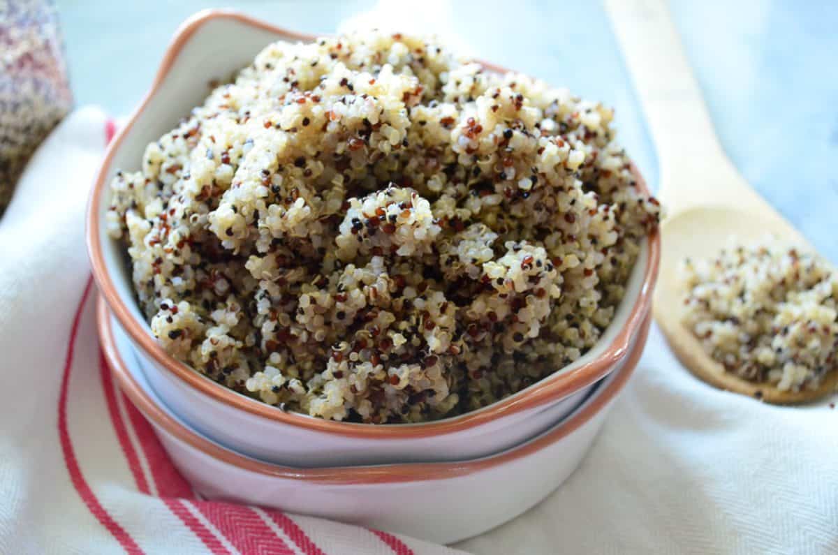 multi-colored cooked quinoa in white bowl with orange rim on cloth with wooden spoon.