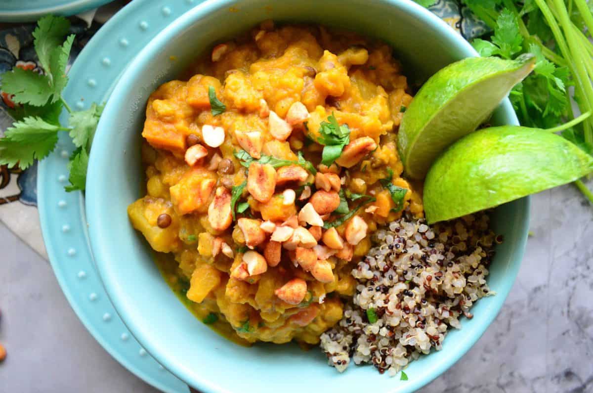 top view blue bowl of lentils with nuts, quinoa, herbs, and lime on top of matching blue plate.