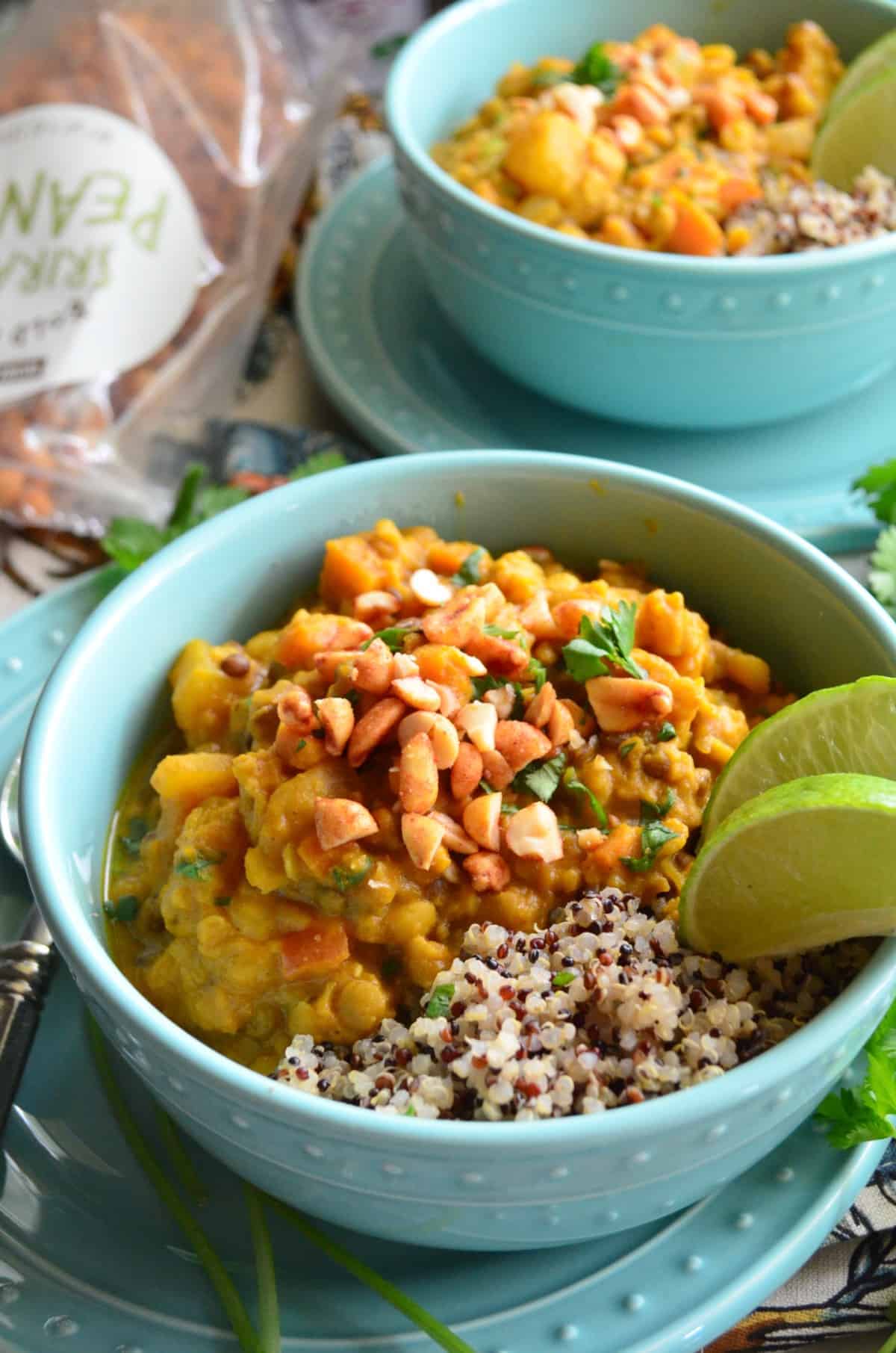 close up top view bowl of lentils with nuts, quinoa, herbs, and lime on top of matching blue plate.