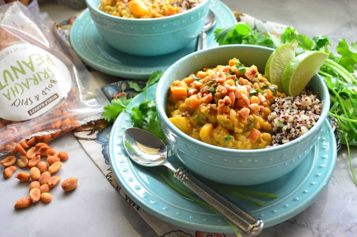 Blue bowl of lentils with nuts, quinoa, herbs, and lime on top of matching blue plate on counter with fresh cilantro.