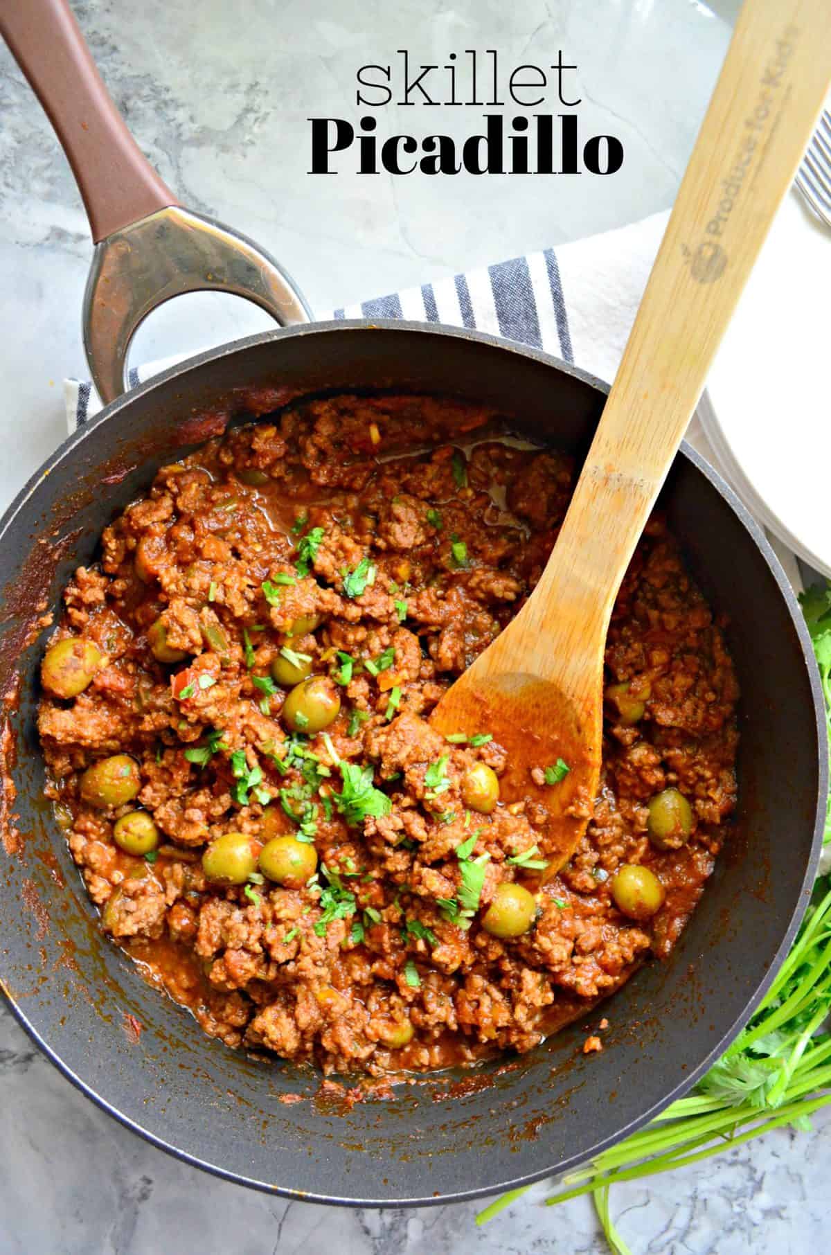 top view of ground meat, red sauce, green olives, and fresh herbs in a skillet with wooden spoon and title text.