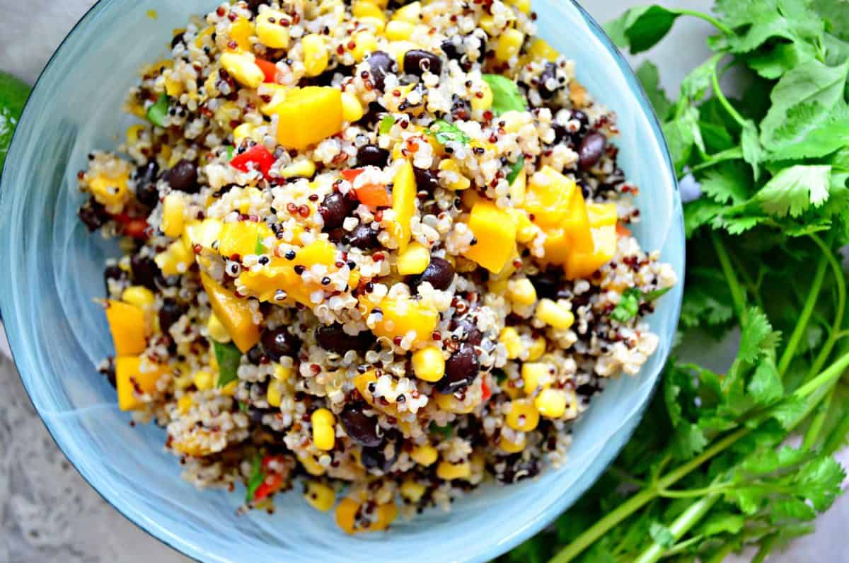 top view of quinoa with corn, peppers, cilantro, and mango in blue bowl next to fresh cilantro.