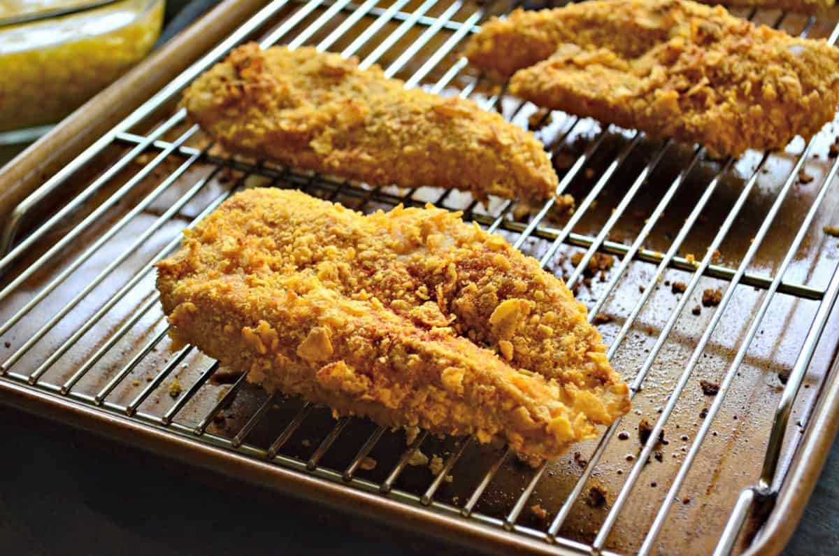 side view 3 chicken pieces coated in corn flakes on rack over top of sheet pan.