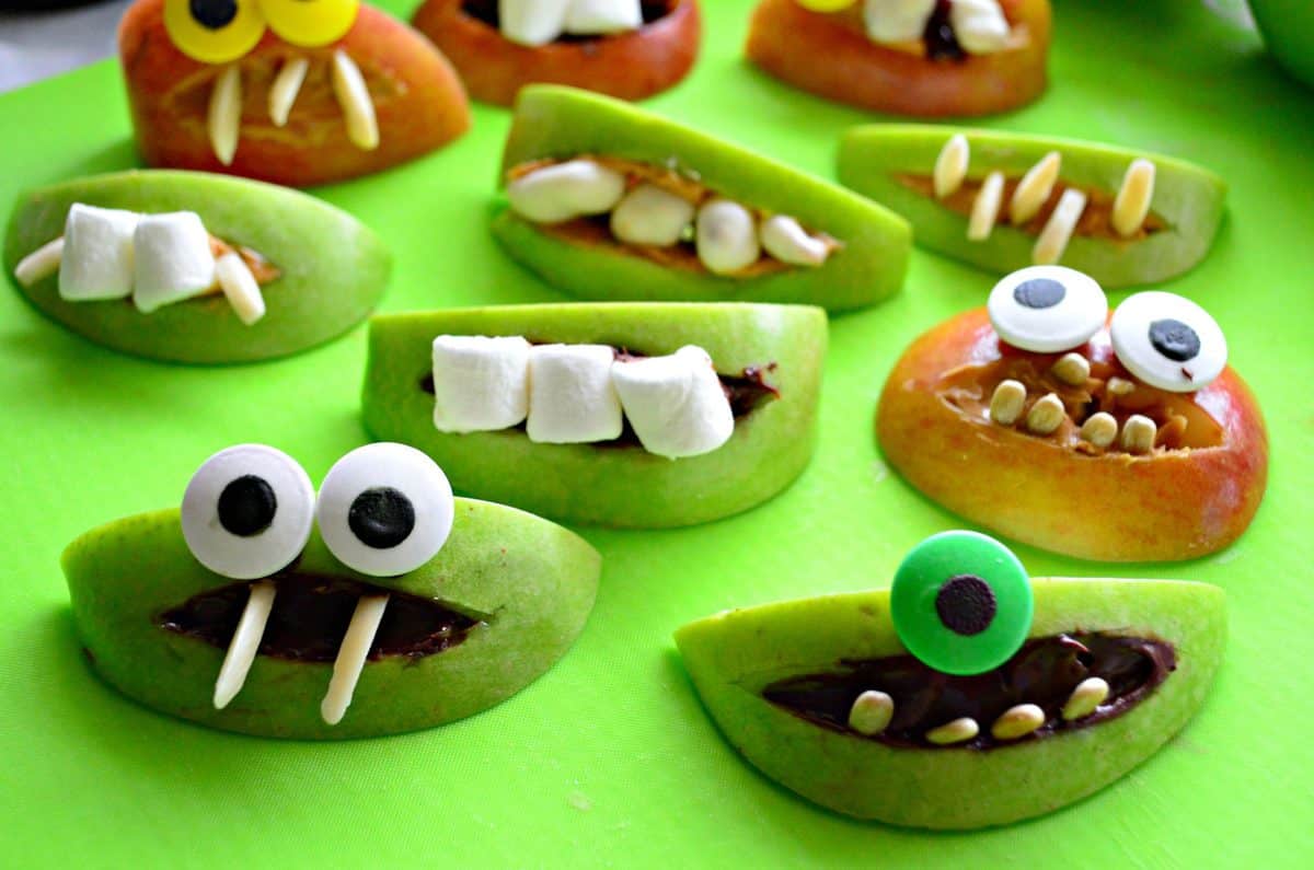 assorted apple slices decorated with peanut butter, nuts, marshmallows, and googly eyes to look like monsters.