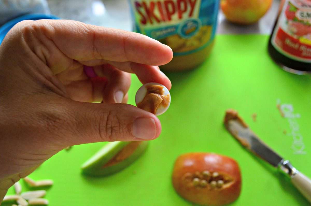 hand holding up candy googly eye with peanut butter spread on the back of it.