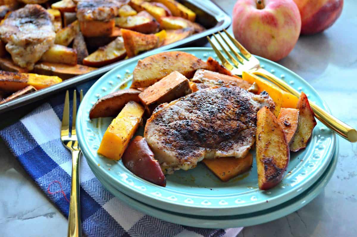 Plated seasoned pork chops, sliced apples, and sliced butternut squash with fork near apples.