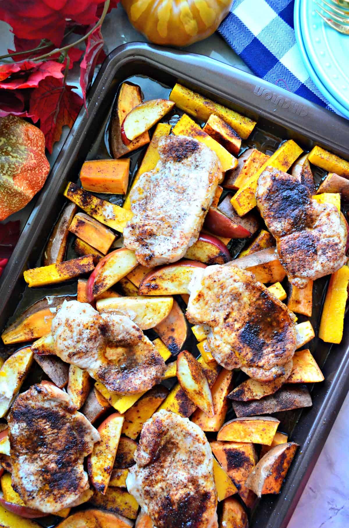 top view of seasoned pork chops, sliced apples, and sliced butternut squash on sheet pan.