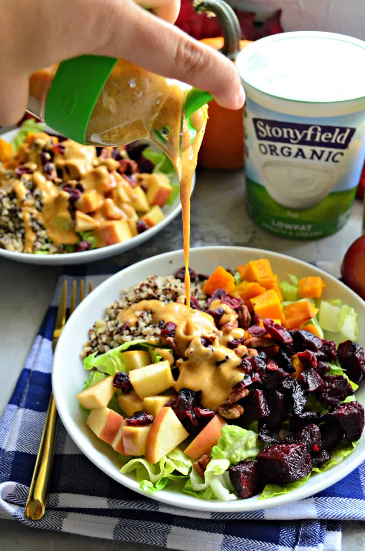 hand holding homemade dressing container over salad as orange colored dressing drizzles down on top of dish.