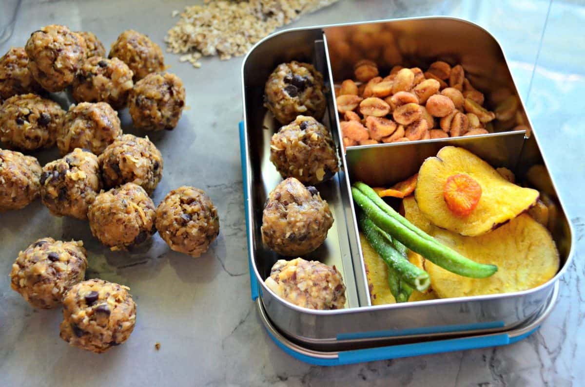 Peanut Butter Chocolate Chip Protein Balls on countertop next to lunch container with nuts and veggies.