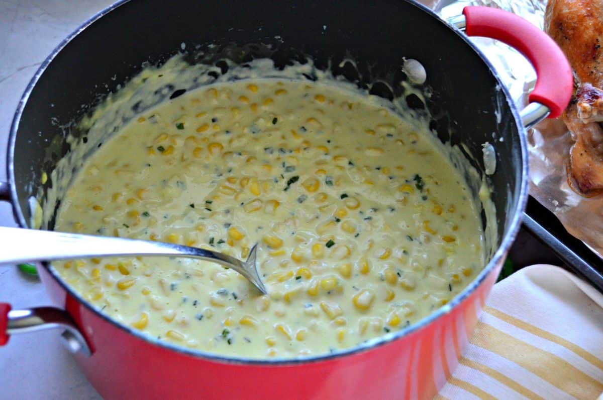creamy corn with pepper and herbs in a red pot with long silver spoon.