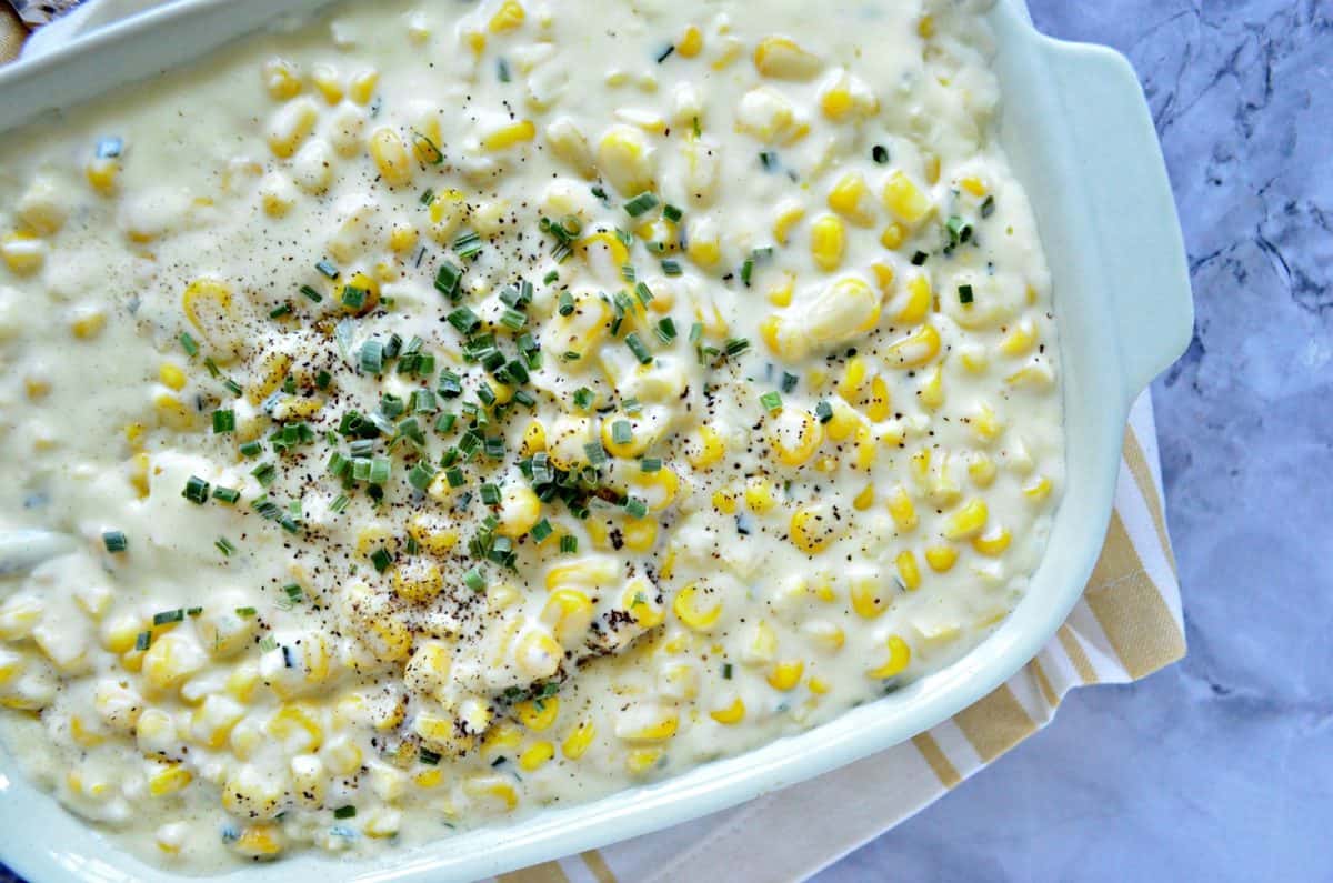 top view of creamed corn in casserole dish topped with herb sand pepper on countertop.