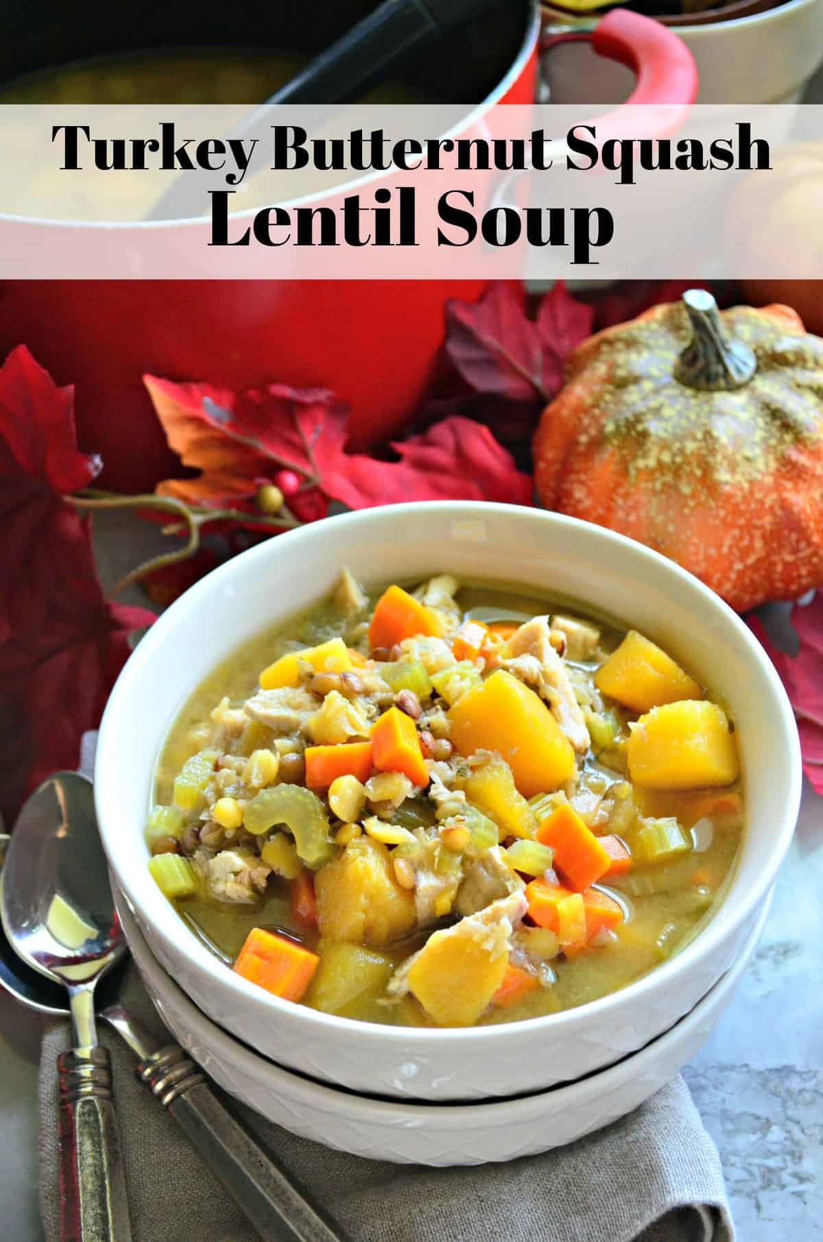 Turkey Butternut Squash and Lentil Soup in white bowl on table with fake decorative fall leaves and title text.