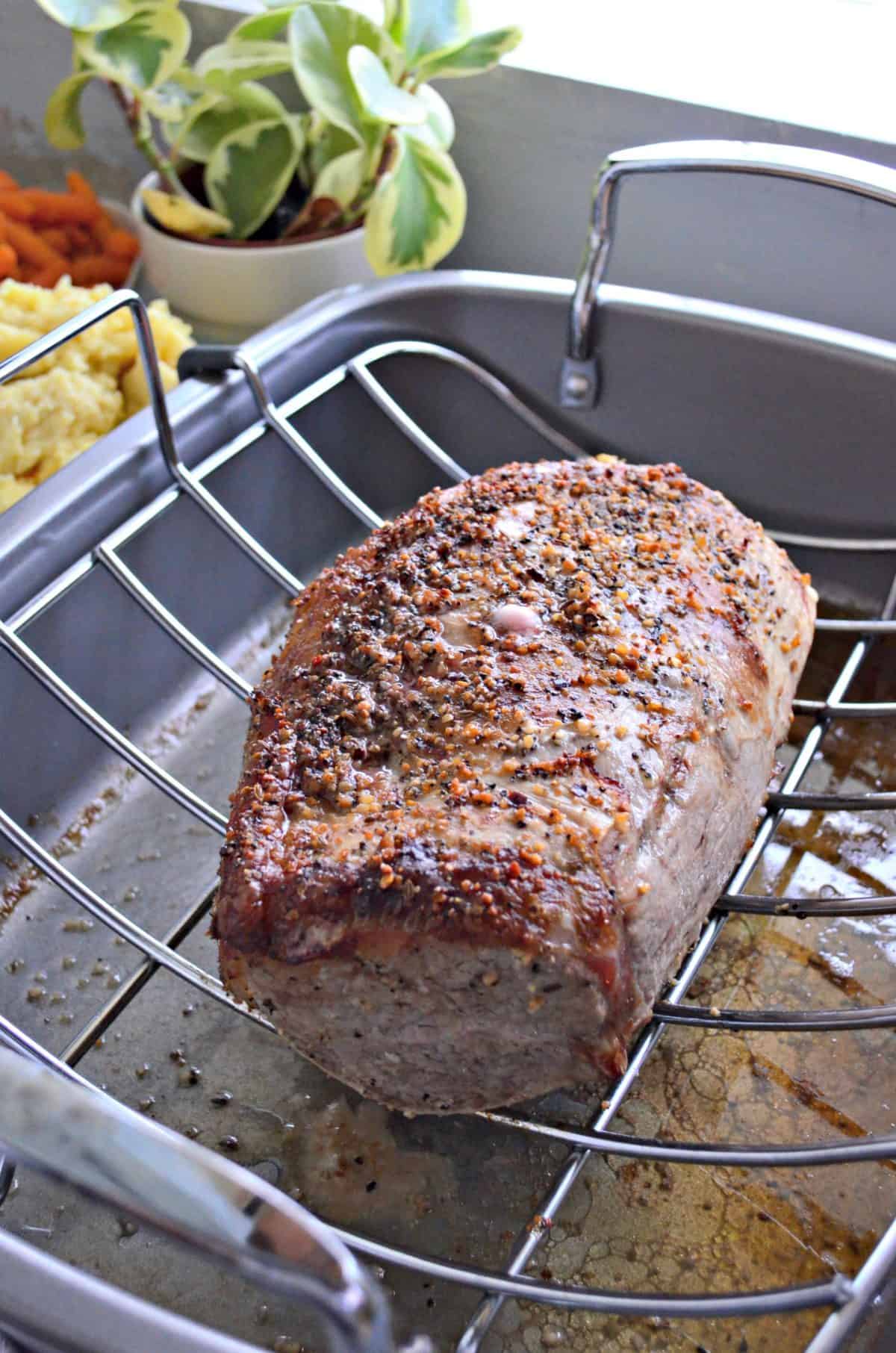 whole roast beef crusted with spices on silver resting rack in large pan with juices dripping below rack.