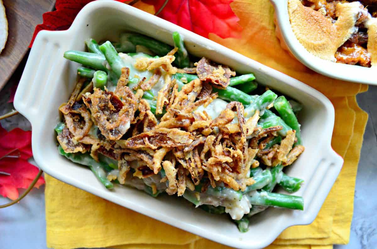 Top view small casserole dish of green beans with white chunky substance topped with crispy onions. 