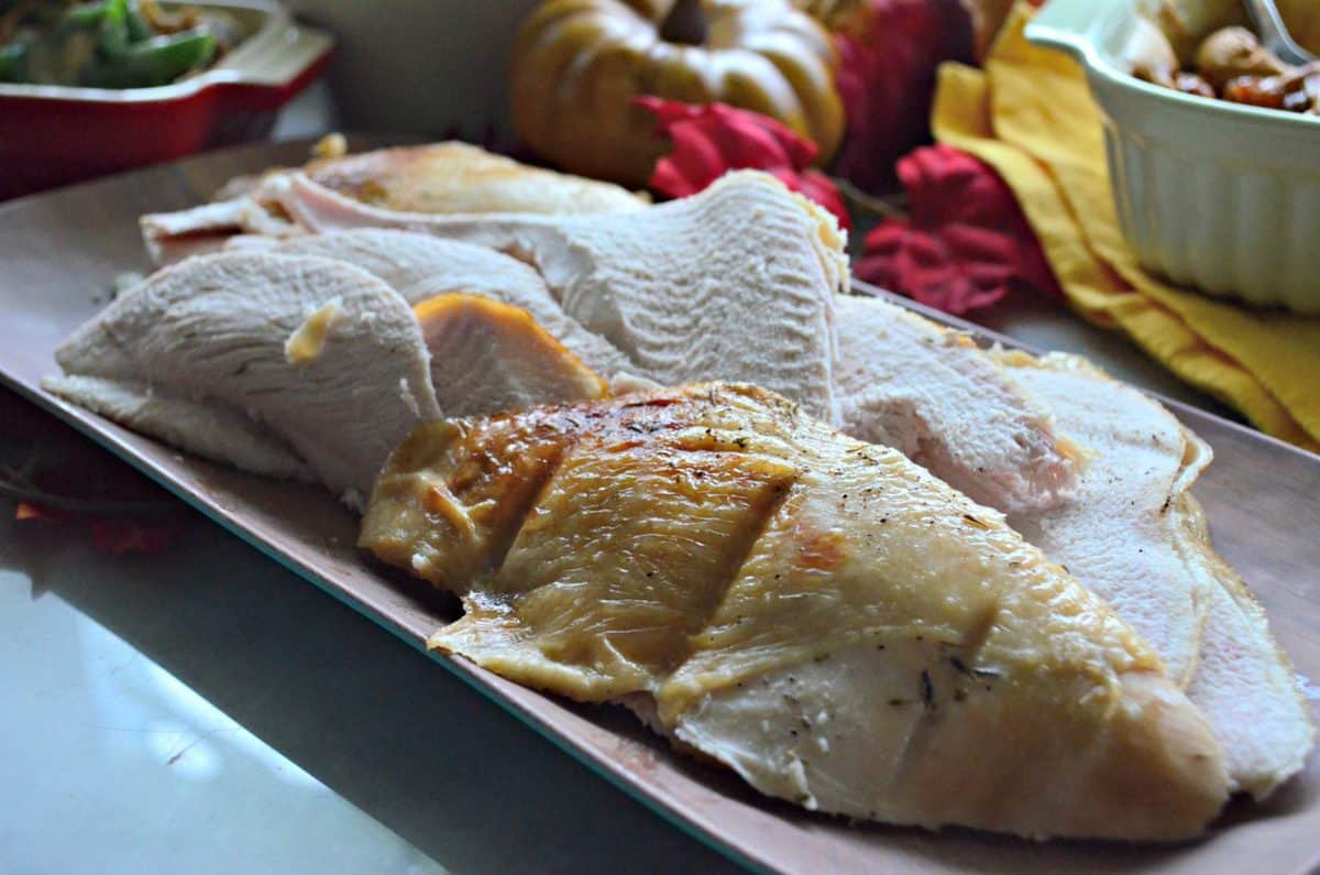 side view of sliced and cooked Garlic & Thyme Turkey Breast on rectangular platter in front of fall decor.