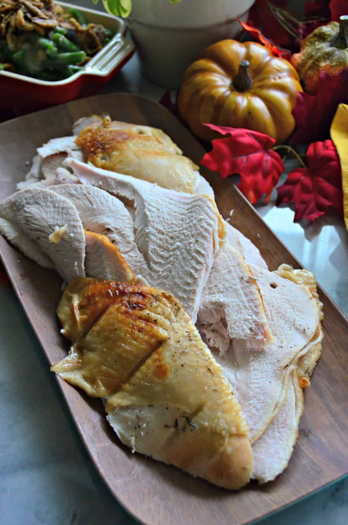 top view of sliced turkey breast on rectangular platter next to green bean casserole and fall decor.