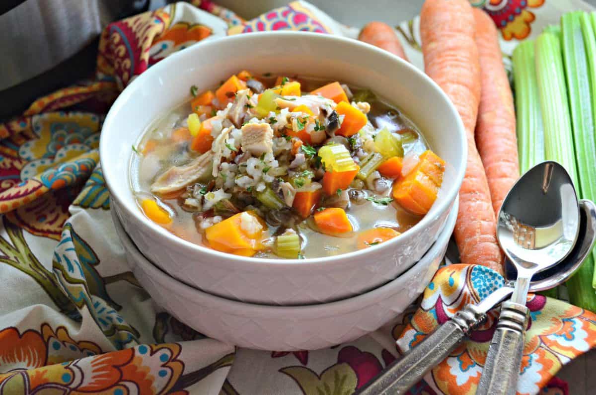 soup in a white bowl with broth, celery, carrots, rice, herbs, and turkey on a tablecloth.