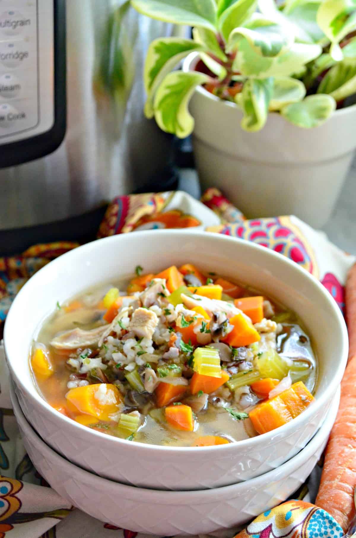 closeup of soup in a white bowl with broth, celery, carrots, rice, herbs, and turkey on a tablecloth.