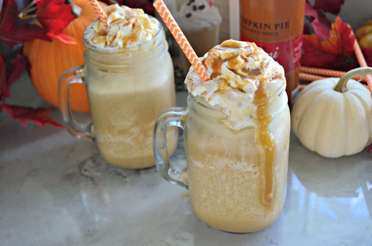 2 mason jar glass mugs with handle filled with light orange frozen drink topped with whipped cream and caramel.