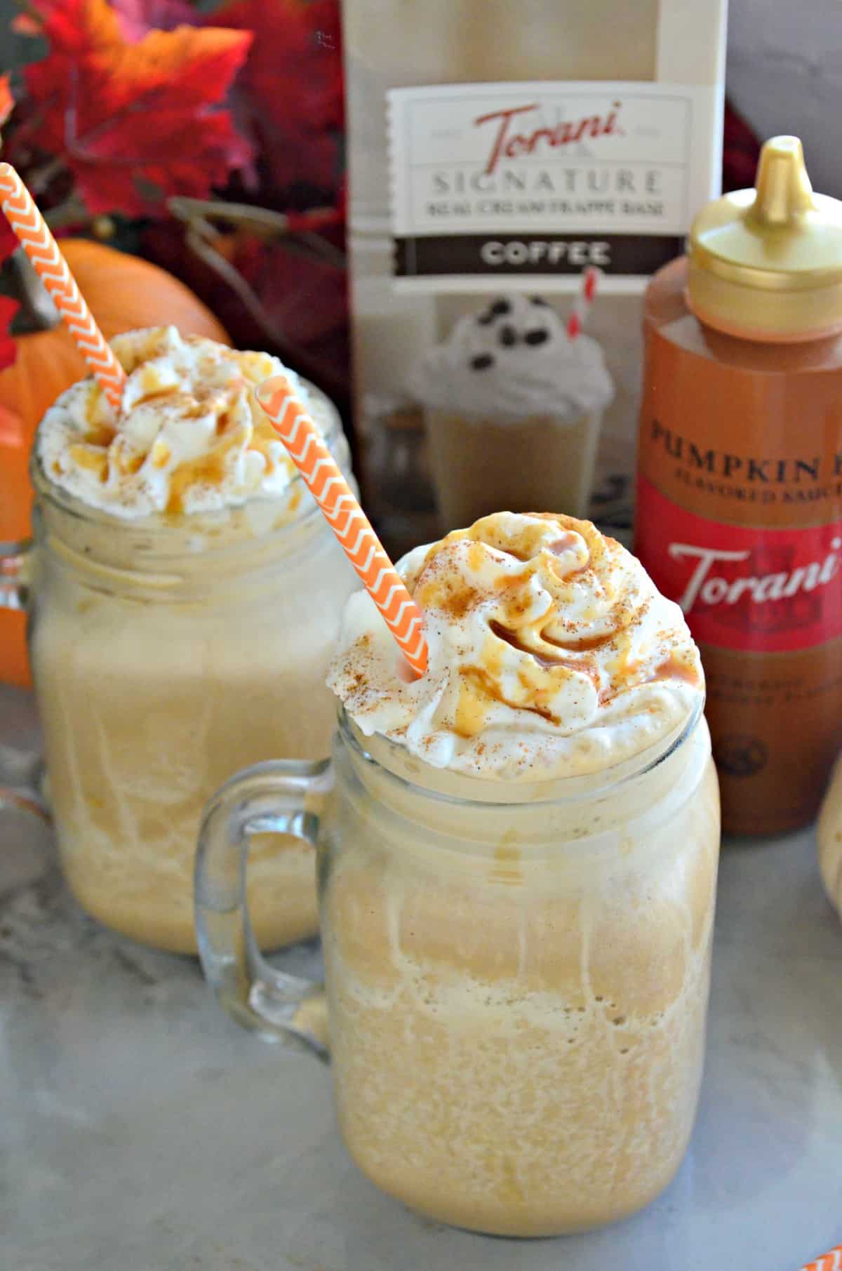 2 mason jar glass mugs with handle filled with frozen drink topped with whipped cream and caramel.