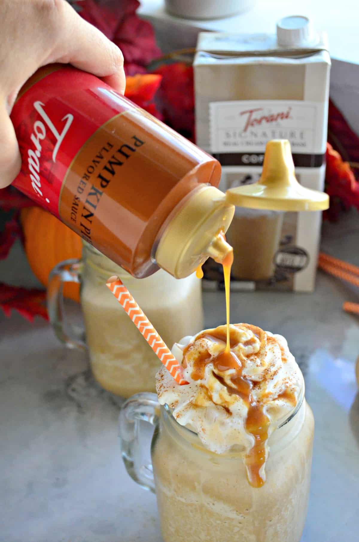 hand holding bottle of torani pumpkin pie flavored sauce as it drizzles over whipped cream on frappe.