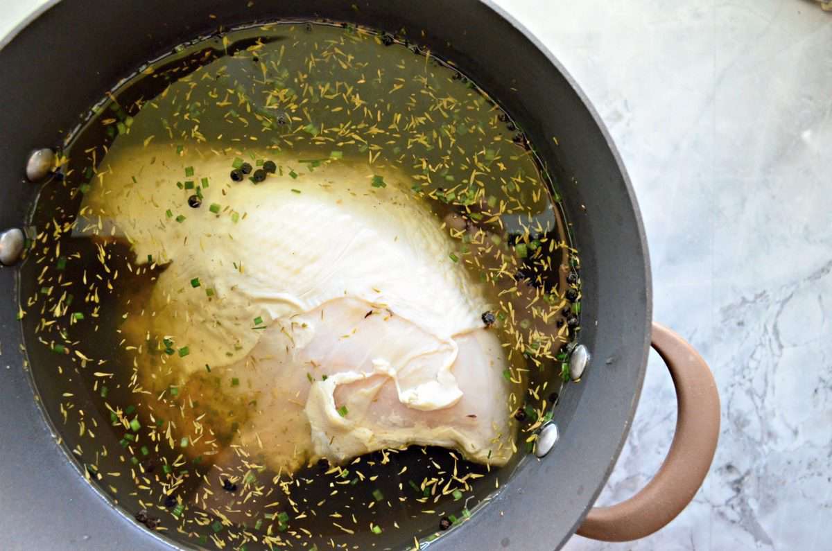 top view of raw Turkey brining in yellowish liquid with herbs in pot.