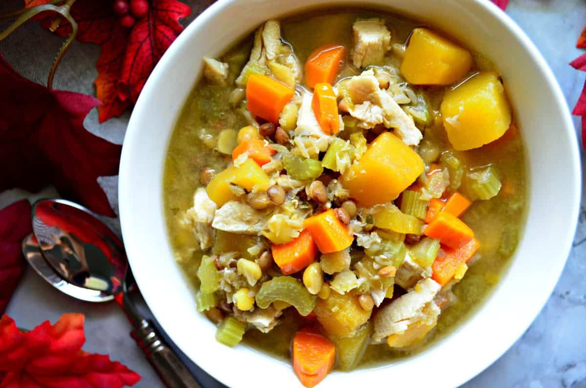 Top view of Turkey Butternut Squash and Lentil Soup in white bowl on table with fake decorative fall leaves.