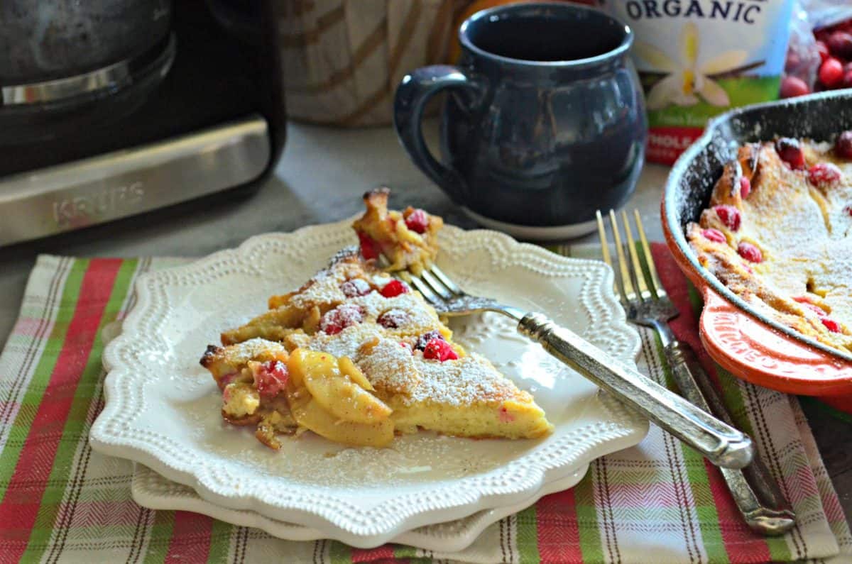 plated slice of pancake pastry with apples and cranberries baked in topped with powdered sugar.