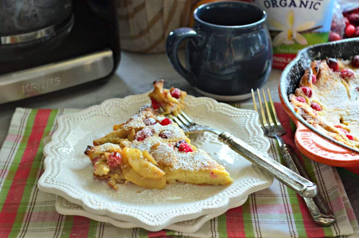 plated slice of pancake  pastry with apples and cranberries baked in topped with powdered sugar.