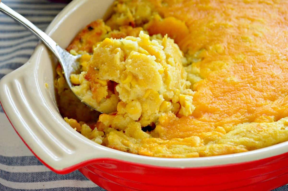 closeup of Double Cream Corn Casserole in red baking dish with spoon scooping out a bite.