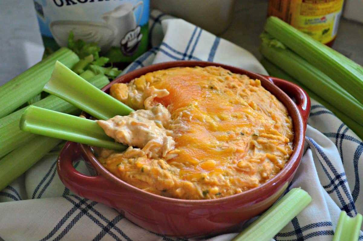 2 celery sticks sticking out of thick orange dip topped with melted cheese in small red bowl.