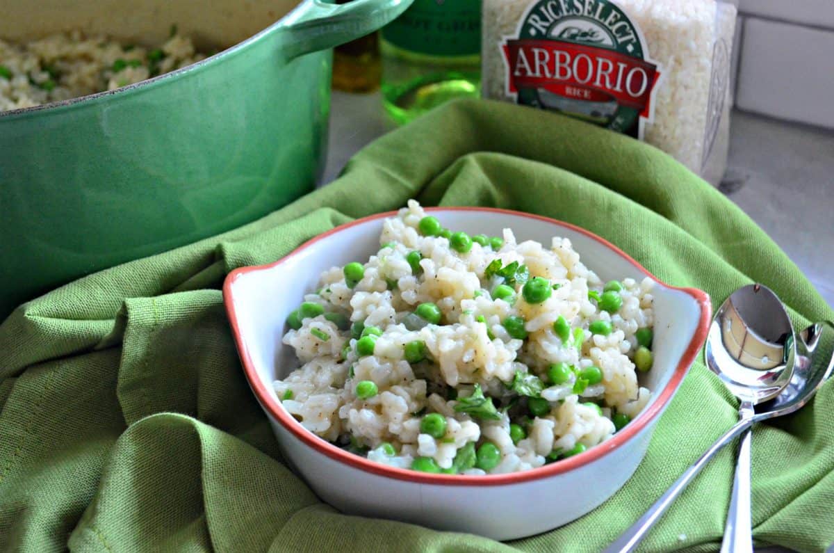 Baked Risotto with Green Peas and pepper in small white bowl on green tablecloth with two spoons.