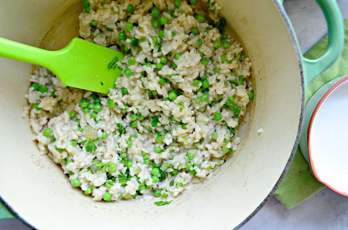 top view of Baked Risotto with Green Peas in pot being stirred with spatula.