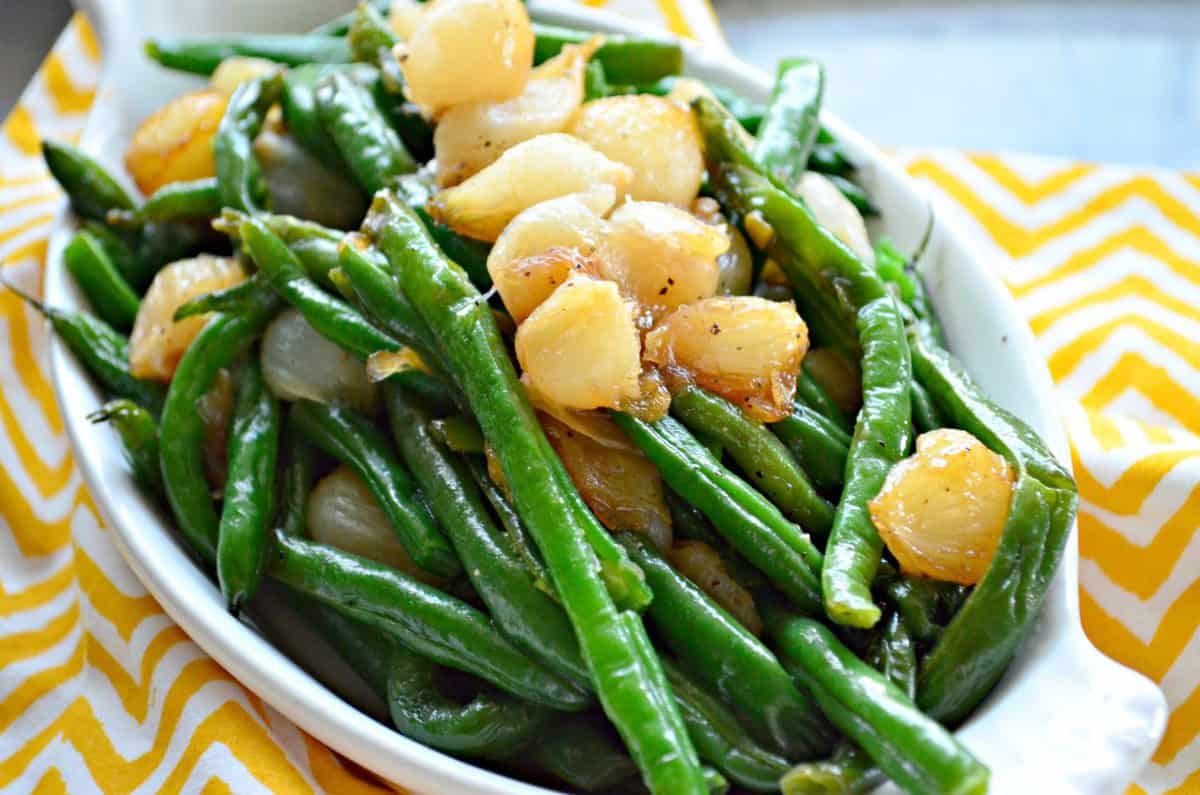 Green Beans with Caramelized Pearl Onions in oval ceramic dish on yellow and white chevron tablecloth.