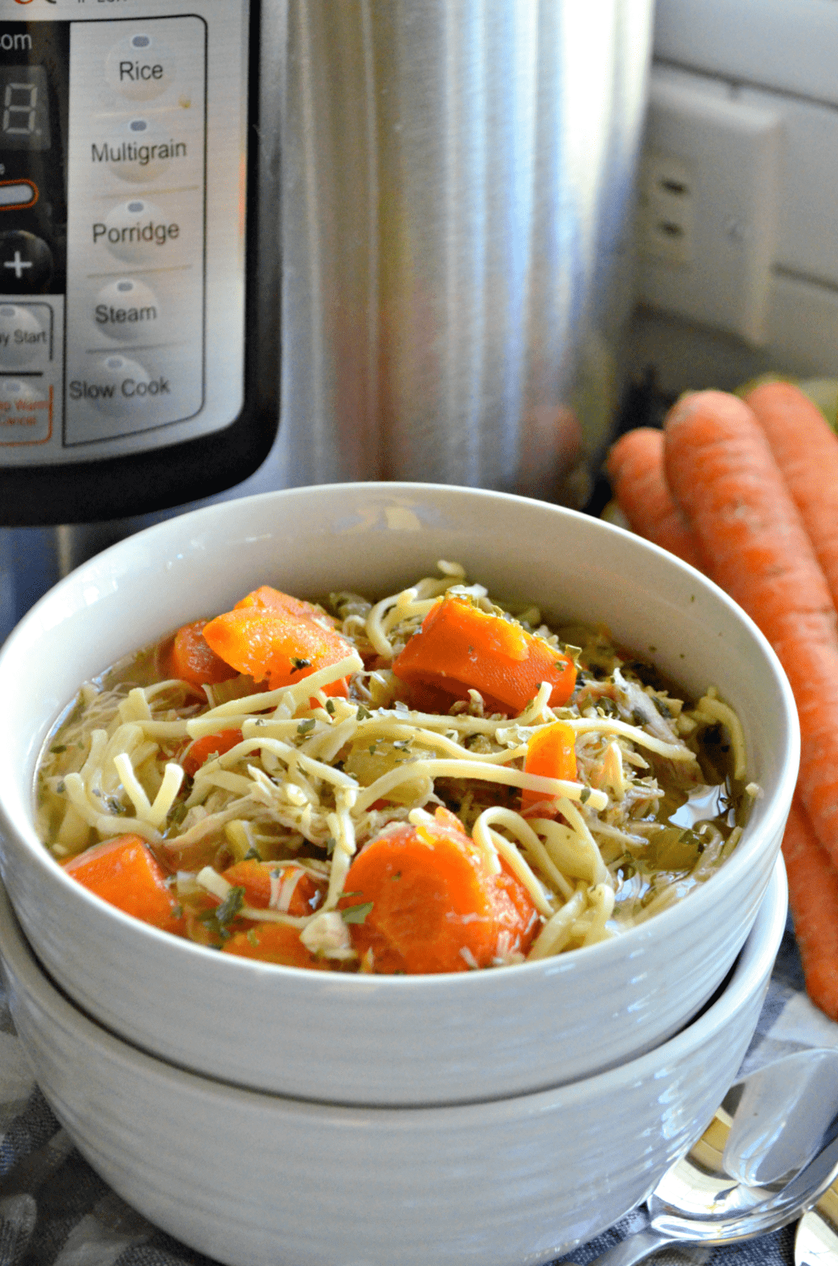 close up bowl of chicken noodle soup with carrots and celery in it in front of fresh carrots.