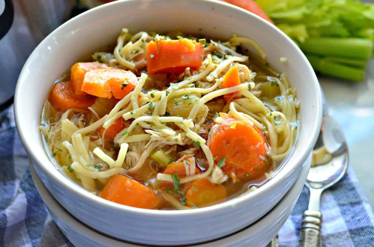 top view of bowl of chicken noodle soup with carrots and celery in it on tablecloth.